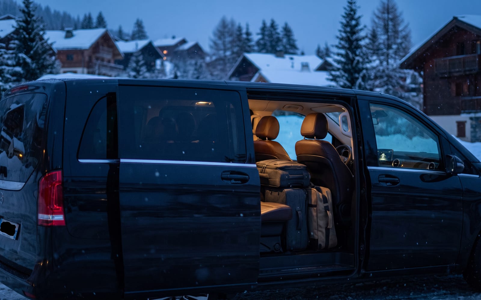 Black Sprinter, side door open onto a lit cabin, skis and luggage stowed